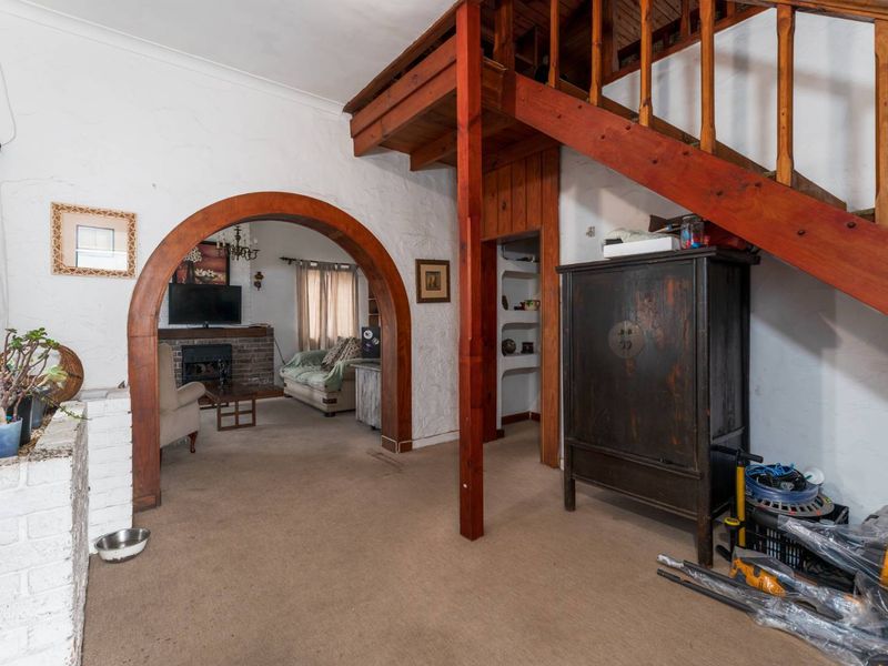 Living area featuring a brick fireplace, arched architectural detail, and a timber staircase leading to an upper level.