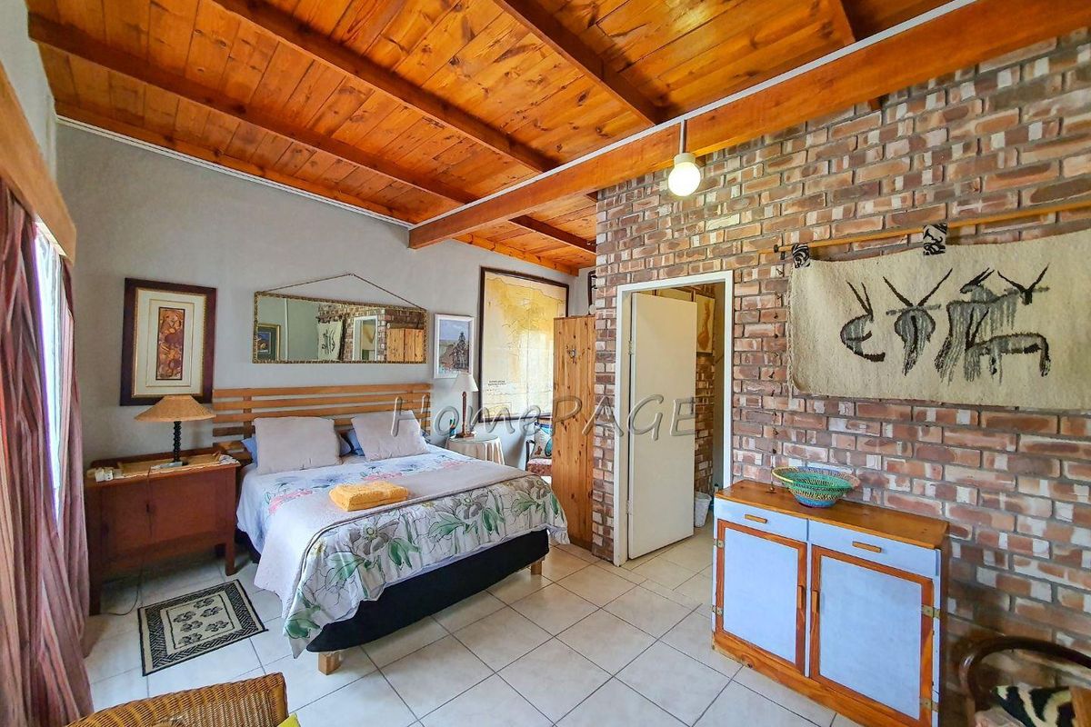A rustic bedroom featuring a vaulted timber-beamed ceiling, exposed brick feature wall, and tiled flooring.