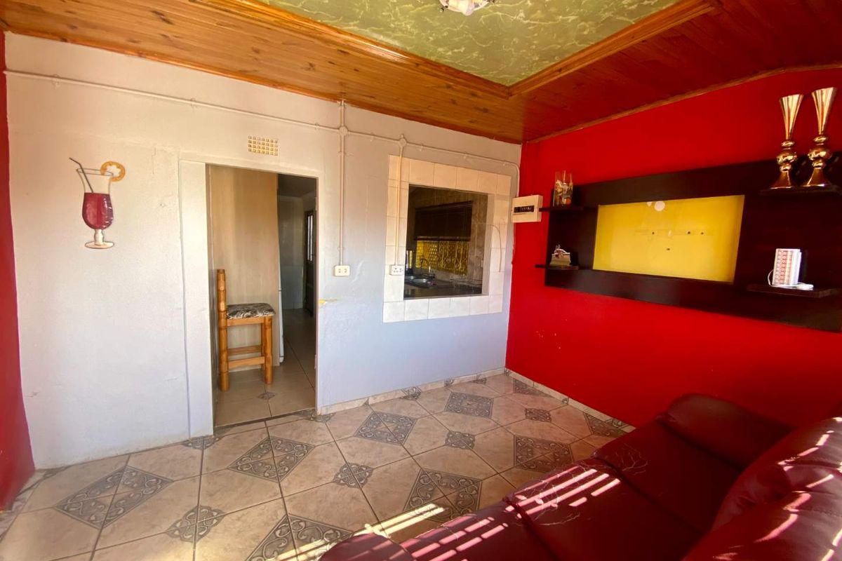 A living room featuring tiled flooring, a timber-paneled ceiling, and a service window connecting to the kitchen area.