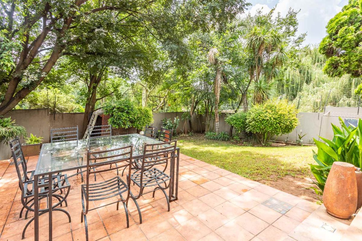 A private rear garden featuring a paved patio area, established trees, and a lawn, providing a tranquil outdoor space for relaxation.