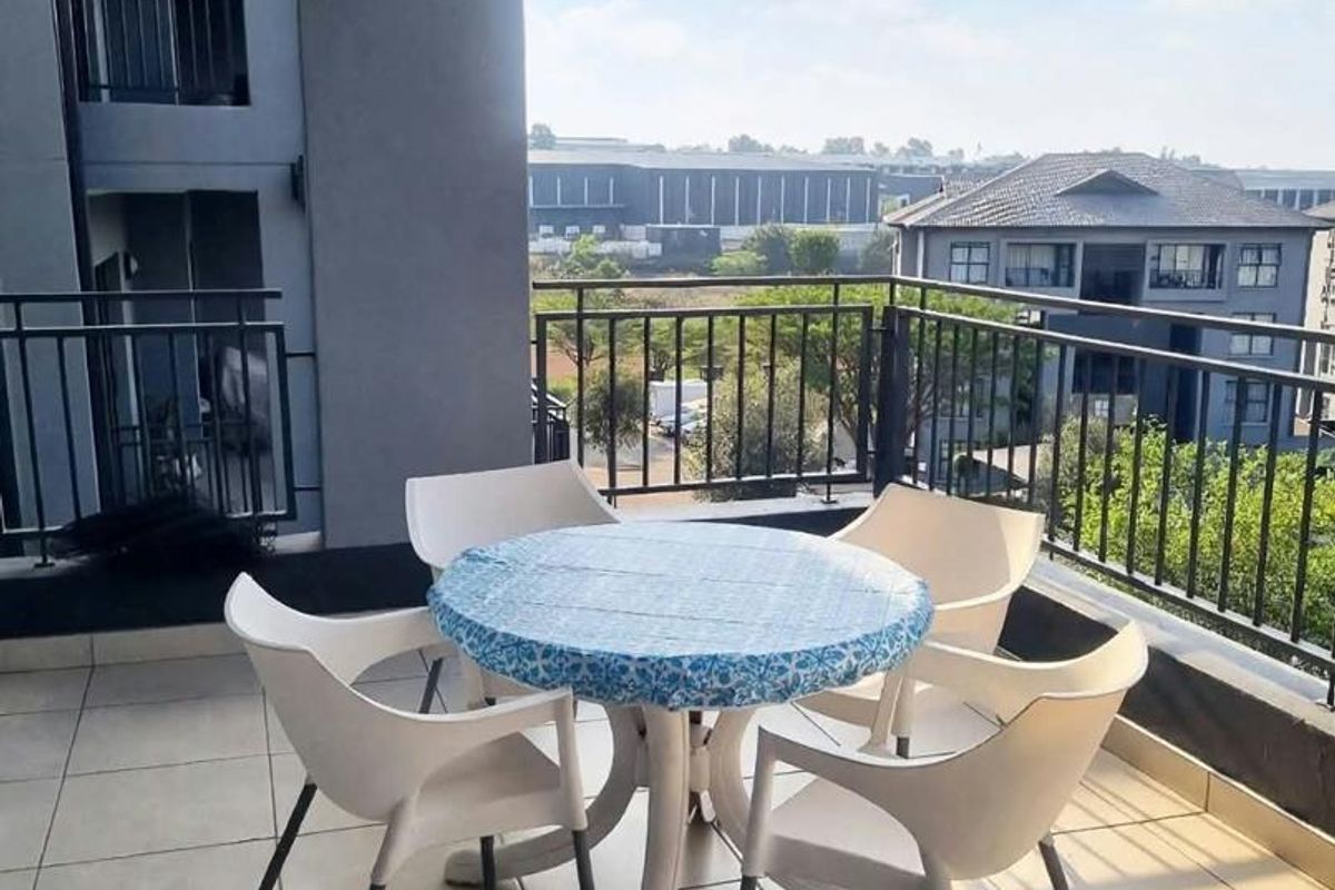 A spacious covered balcony featuring tiled flooring and a metal balustrade, offering an open view of the surrounding residential complex.