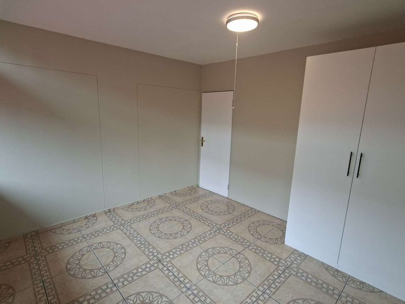 A clean, empty bedroom featuring tiled flooring, a built-in wardrobe, and neutral wall tones, offering a blank canvas for personalization.