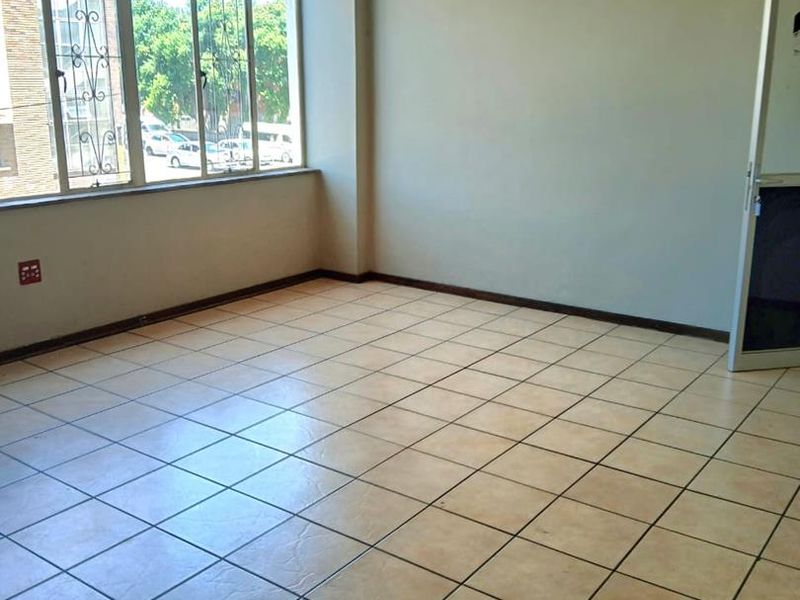 A bright, empty office space featuring neutral tiled flooring and large windows with security bars, offering a clean and functional workspace.