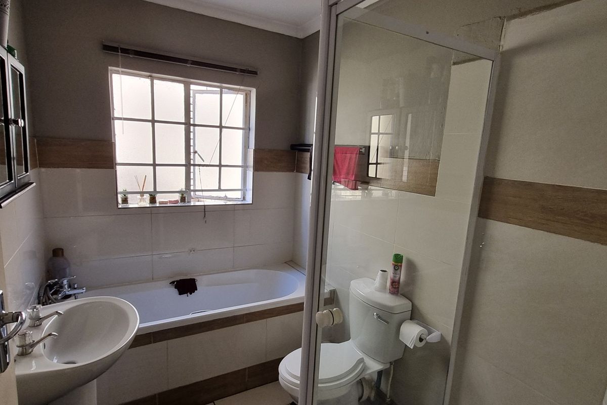A functional bathroom featuring a bathtub, separate shower enclosure, pedestal basin, and toilet with neutral wall tiling.