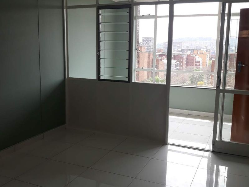 An empty living area featuring polished tiled floors, a glass partition wall with louvre windows, and access to an attached balcony with city views.