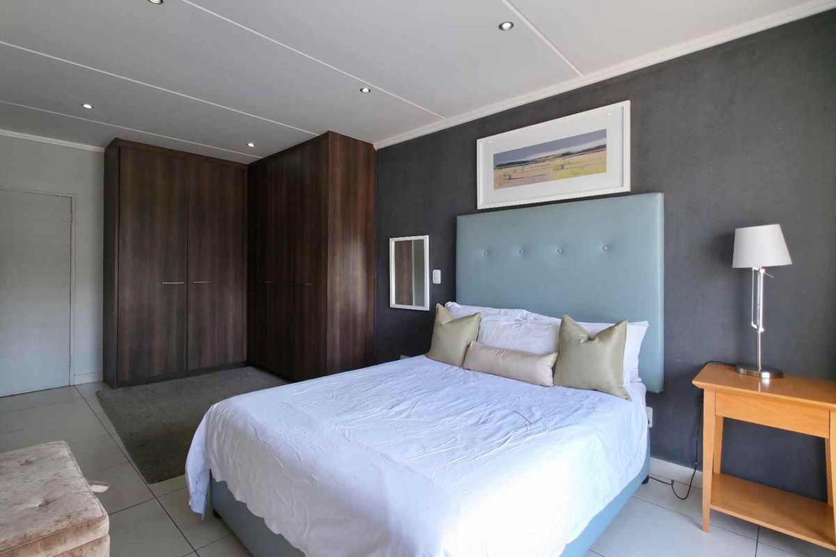 A well-maintained bedroom featuring built-in dark wood cabinetry, tiled flooring, and a modern accent wall with recessed ceiling lighting.