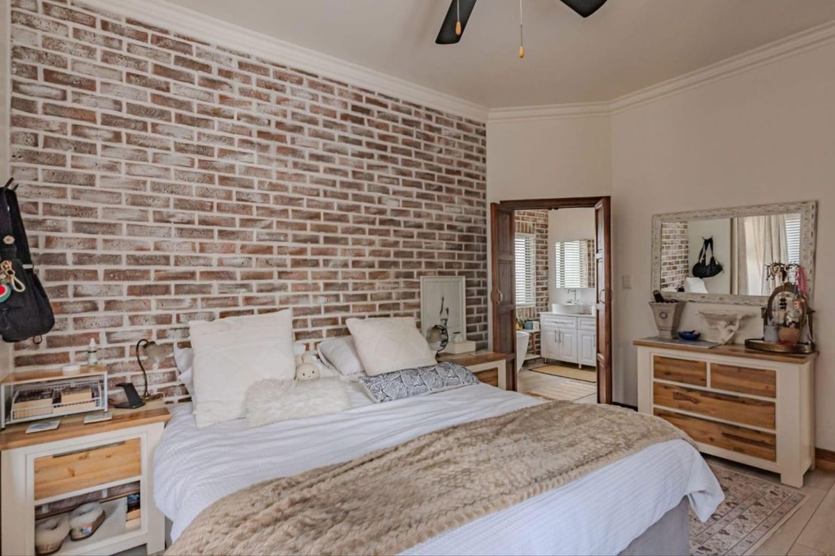 Spacious bedroom featuring a rustic exposed brick feature wall, crown molding, ceiling fan, and direct access to an en-suite bathroom.