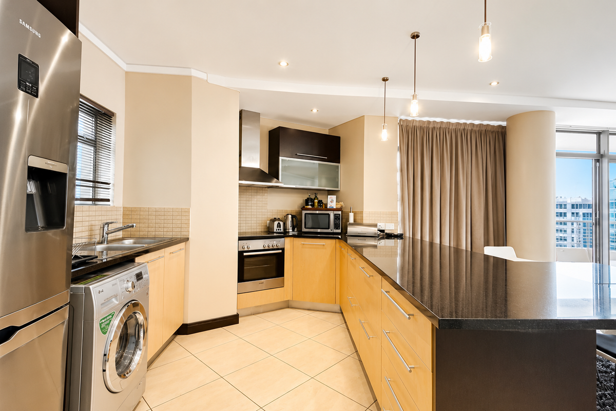 Modern kitchen featuring light wood cabinetry, granite countertops, stainless steel appliances, and a breakfast bar, seamlessly integrated into an open-plan living space.