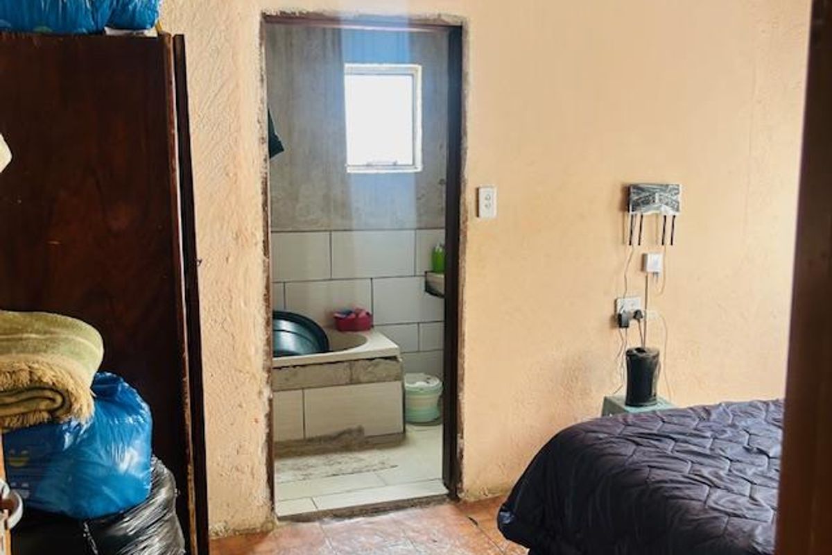 A bedroom featuring tiled flooring and direct access to an adjoining bathroom, currently requiring significant cosmetic updates and wall repairs.
