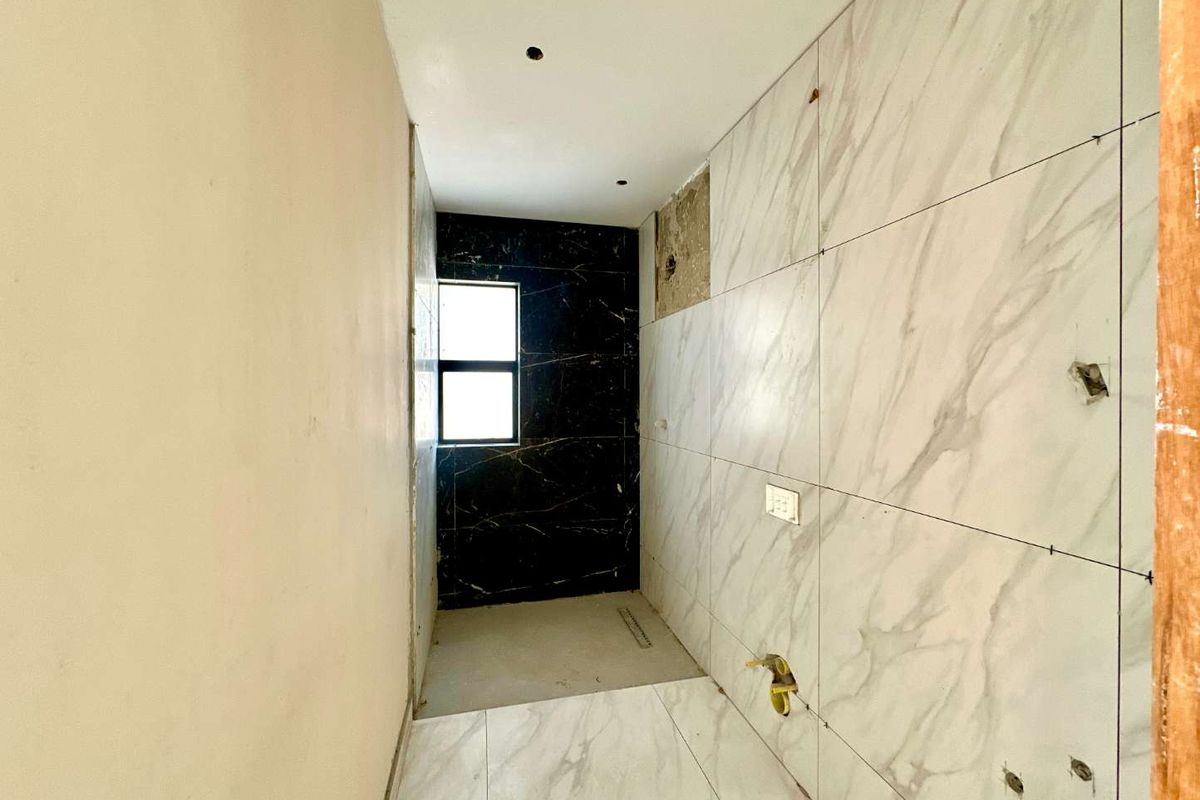 An unfinished bathroom space featuring marble-look wall tiles, a black feature wall, and plumbing rough-ins, currently awaiting final installation and completion.