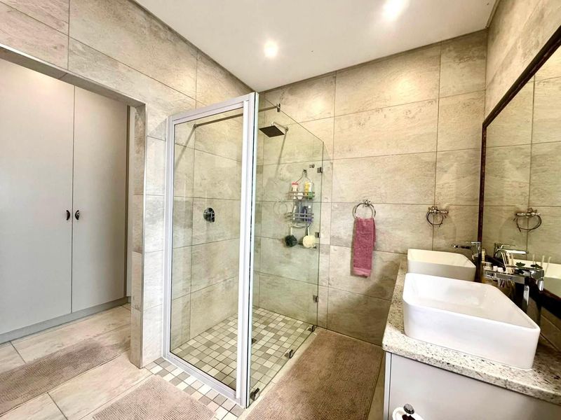 Modern bathroom featuring a glass-enclosed shower, double vanity with vessel sinks, stone countertops, and neutral floor-to-ceiling tiling.