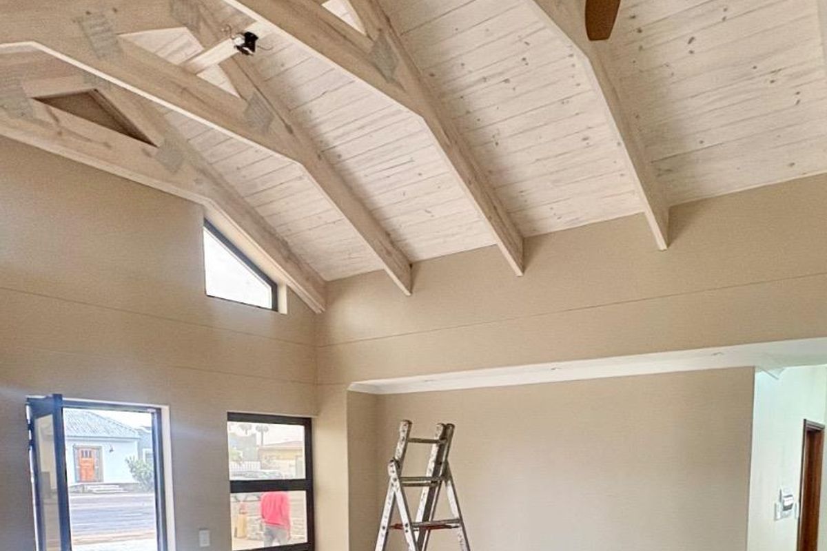 Spacious living area featuring a high vaulted timber ceiling with exposed trusses, ceiling fan, and large windows providing natural light.