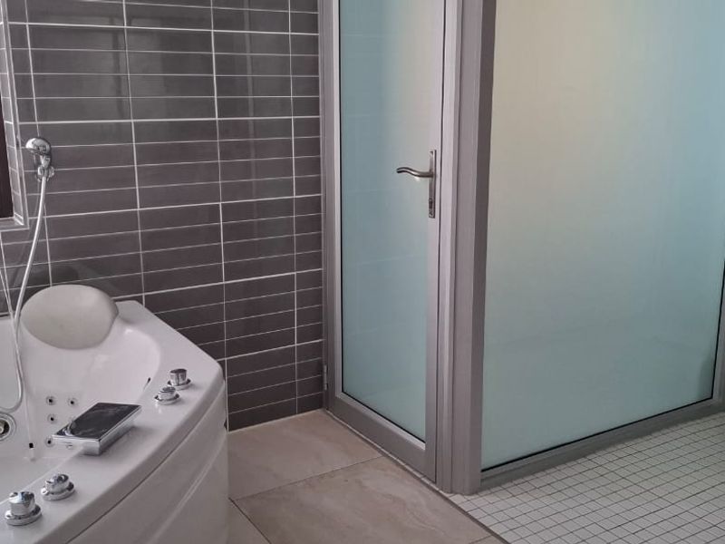 Modern bathroom featuring a corner spa bath, a separate walk-in shower with frosted glass, and contemporary grey wall tiling.