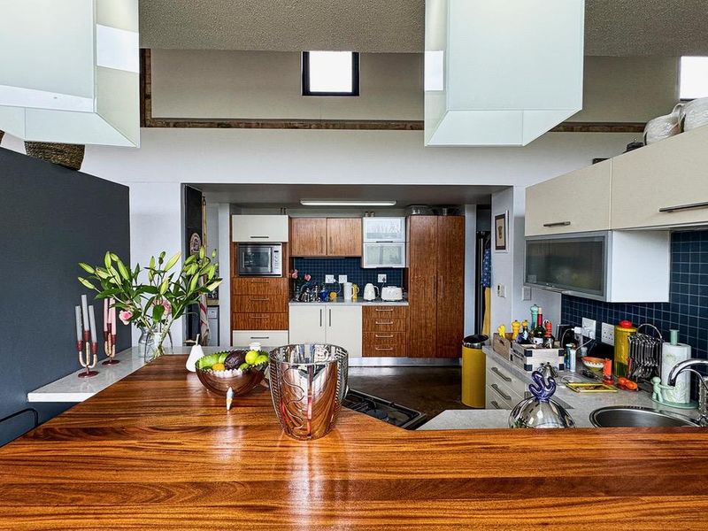 A functional kitchen featuring a large wooden breakfast bar, built-in cabinetry, tiled backsplash, and integrated appliances, illuminated by natural light from a skylight.