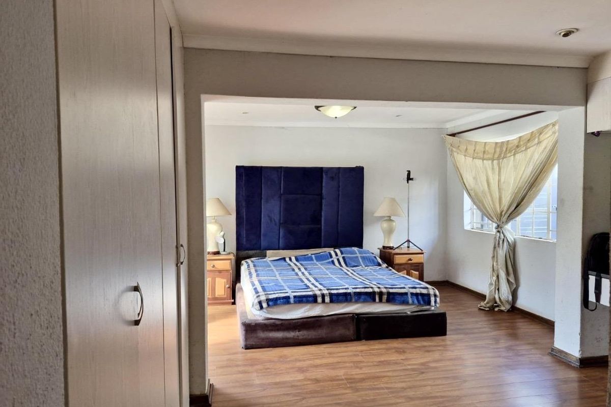 Spacious bedroom featuring built-in cupboards, laminate flooring, and a recessed sleeping area with natural light.