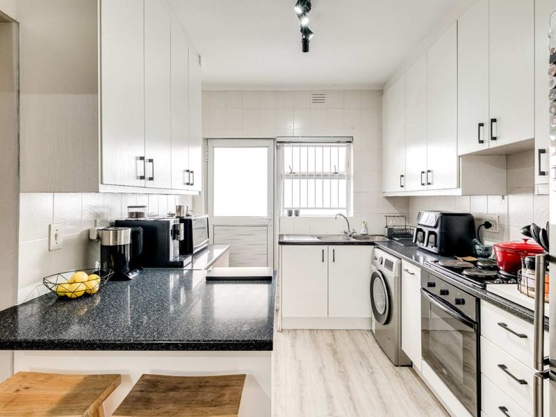 A functional kitchen featuring white cabinetry, dark laminate countertops, built-in oven, electric hob, and integrated laundry plumbing with a tiled backsplash.
