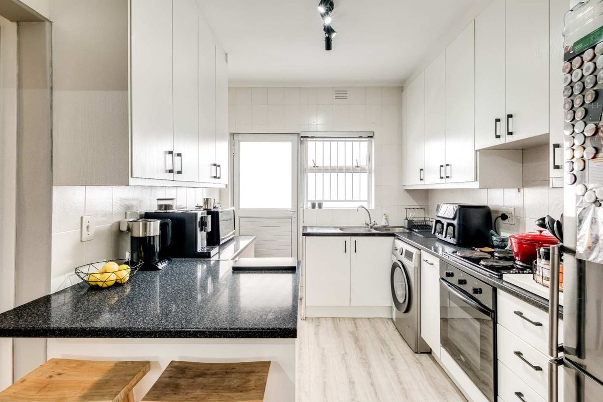 A functional kitchen featuring white cabinetry, dark laminate countertops, built-in oven, electric hob, and integrated laundry plumbing with a tiled backsplash.