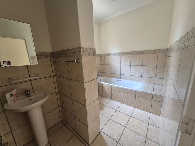 A functional bathroom featuring a pedestal basin, a built-in bathtub, and neutral ceramic tiling throughout.