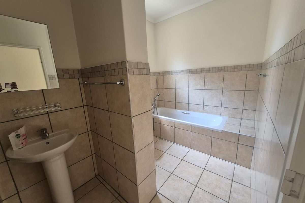 A functional bathroom featuring a pedestal basin, a built-in bathtub, and neutral ceramic tiling throughout.