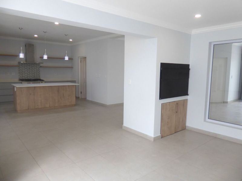 Spacious open-plan living area featuring a modern kitchen with a central island, built-in cabinetry, and neutral tiled flooring throughout.