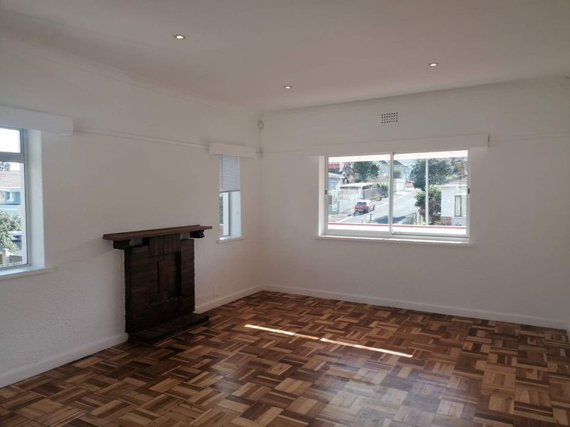 Bright and spacious living room featuring classic parquet flooring, a characterful brick fireplace, and large windows providing natural light.