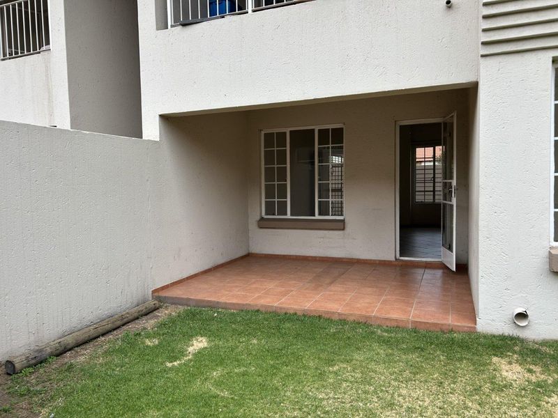 A covered patio area with tiled flooring, providing direct access to the interior through a security gate and overlooking a small private garden space.
