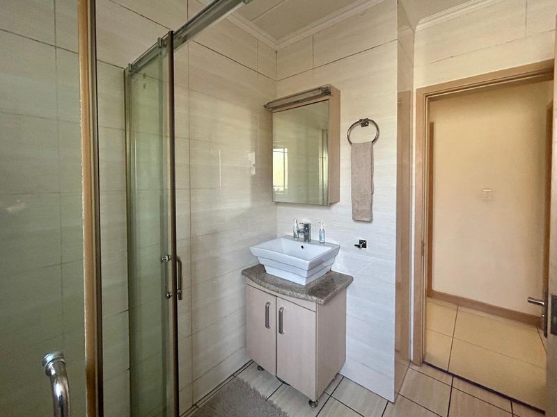 A functional bathroom featuring a glass-enclosed shower, a modern vessel sink with vanity storage, and neutral wall and floor tiling.