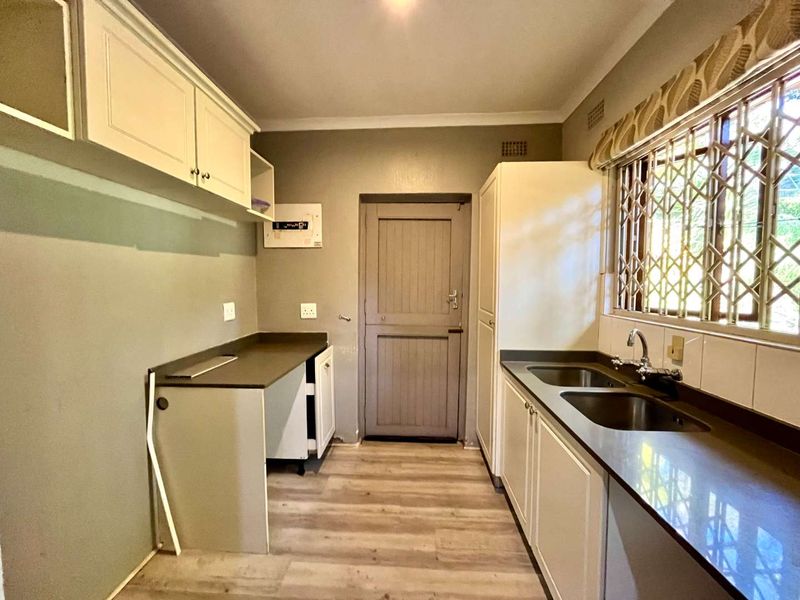 A functional scullery featuring double basin sink, ample built-in cabinetry, laminate flooring, and direct access to the exterior via a secure door.