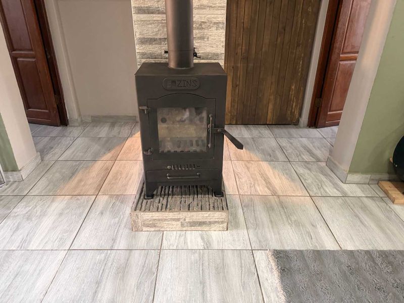 A living area featuring a central freestanding wood-burning fireplace set on a stone-clad hearth with modern wood-look tiled flooring.