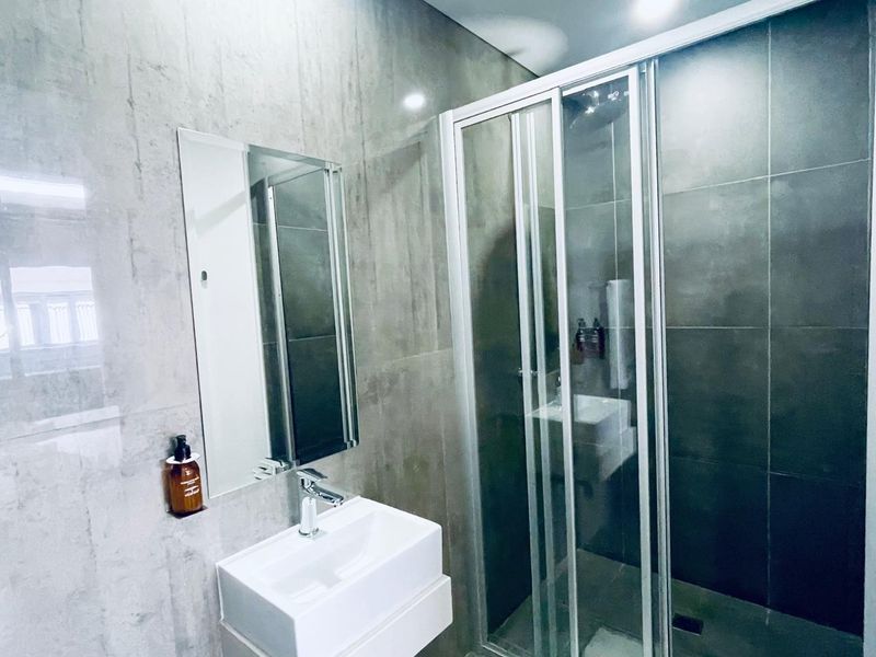 Modern bathroom featuring a wall-mounted vanity basin, chrome fixtures, and a sleek sliding glass shower enclosure with large format tiling.