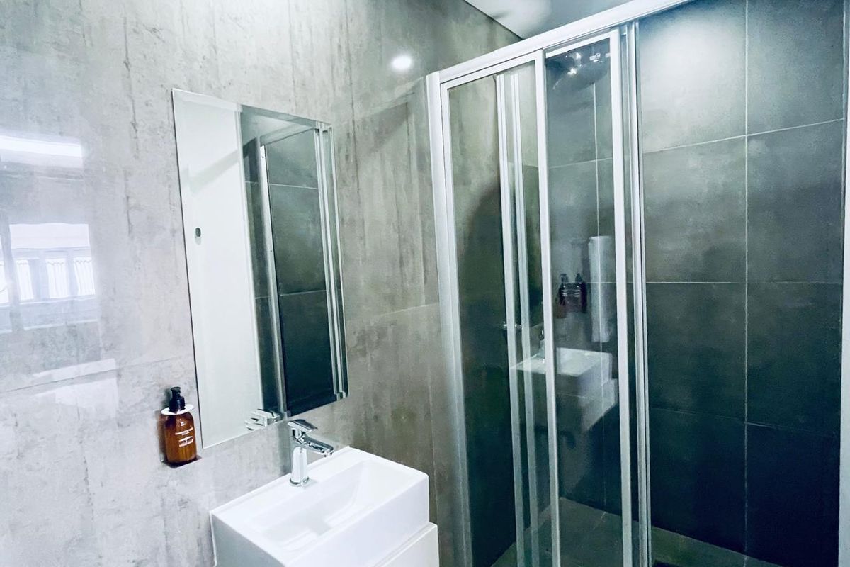 Modern bathroom featuring a wall-mounted vanity basin, chrome fixtures, and a sleek sliding glass shower enclosure with large format tiling.