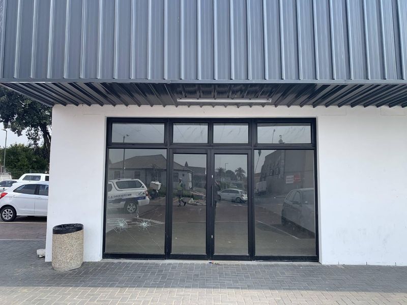 Front facade of a retail unit featuring a metal roof overhang and a large glass storefront entrance with visible damage to the glass.