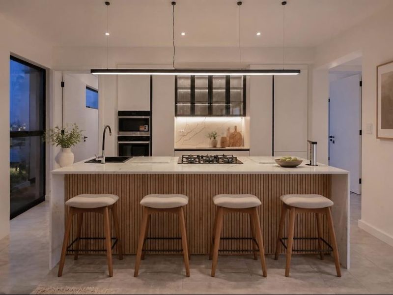 Modern kitchen featuring a large island with stone countertops, integrated gas cooktop, built-in appliances, and stylish slatted timber cabinetry with contemporary pendant lighting.