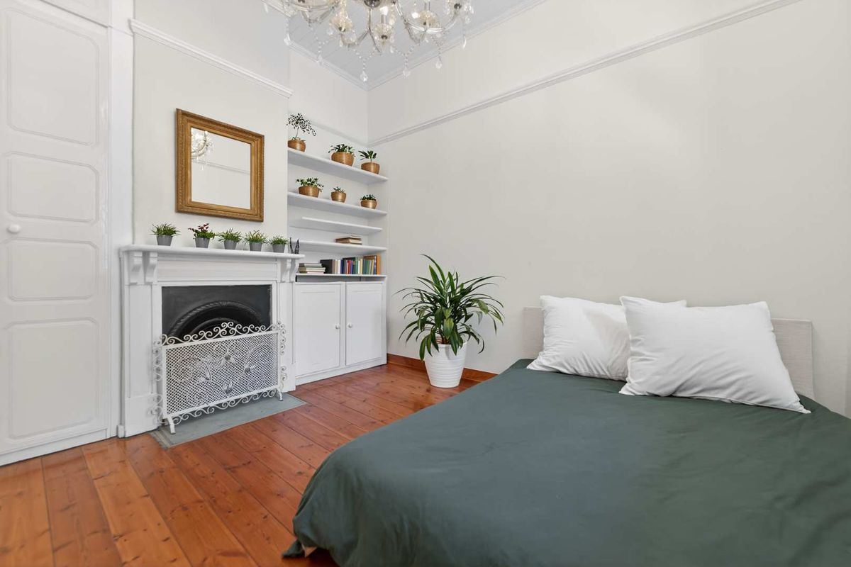 A well-maintained bedroom featuring original timber flooring, a classic fireplace with built-in shelving, and elegant period details including a ceiling rose and chandelier.
