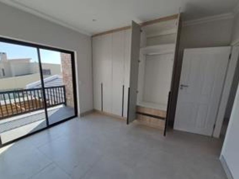 A bright, modern bedroom featuring neutral tiled flooring, ample built-in cupboard space, and a sliding glass door leading to a private balcony.