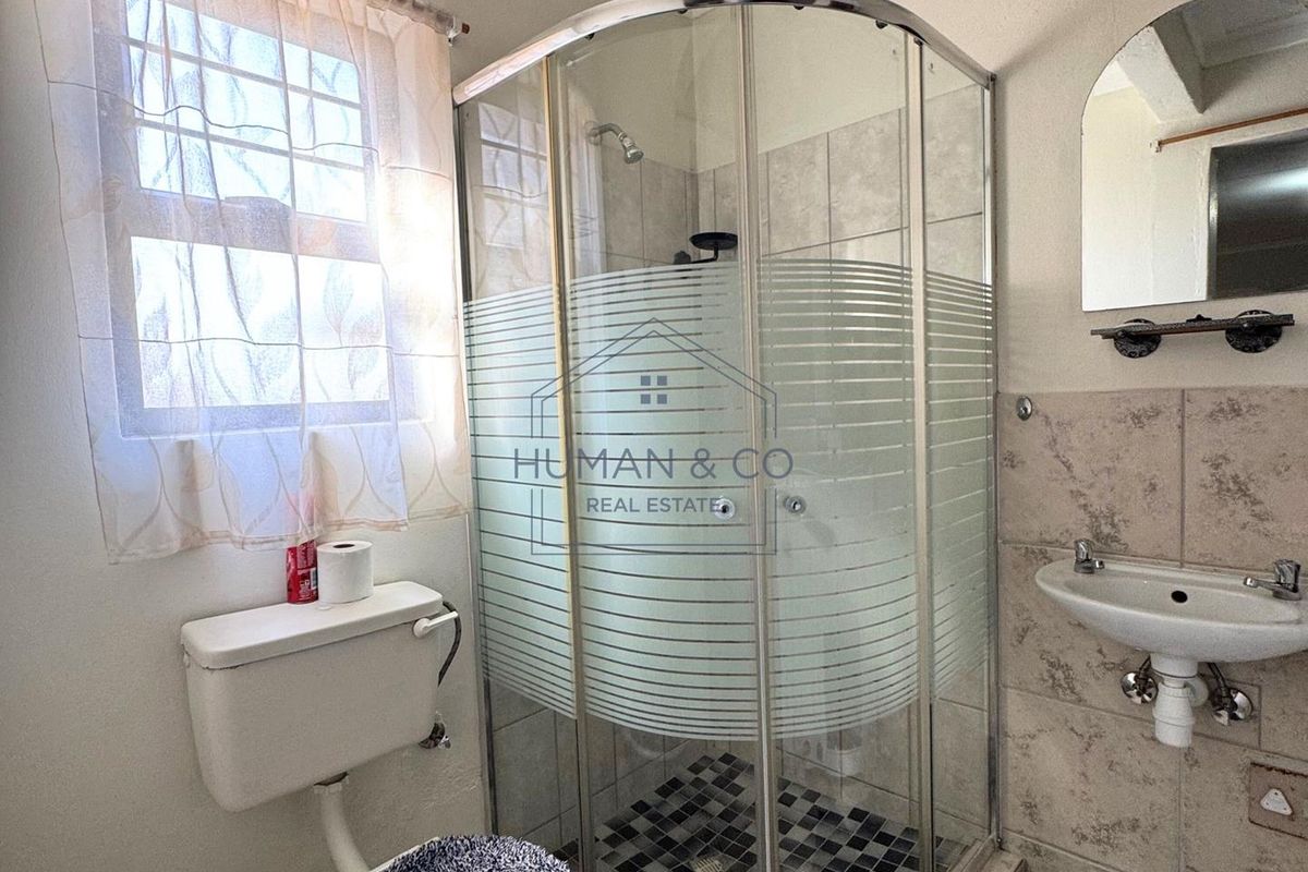 A functional bathroom featuring a corner shower enclosure, wall-mounted basin, and standard toilet, finished with neutral wall tiles.