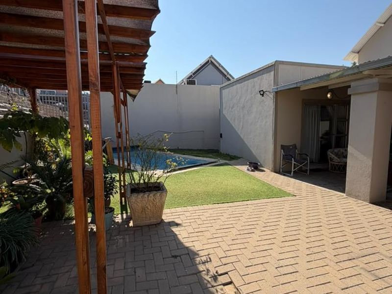 Rear outdoor area featuring a paved patio with a wooden pergola, artificial lawn, and a swimming pool enclosed by boundary walls.