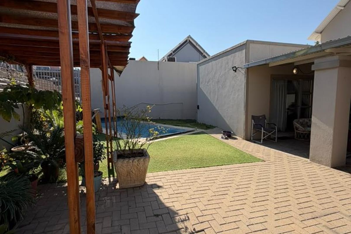 Rear outdoor area featuring a paved patio with a wooden pergola, artificial lawn, and a swimming pool enclosed by boundary walls.
