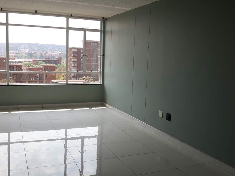 An empty living room featuring polished white floor tiles, a large window with city views, and a painted accent wall.