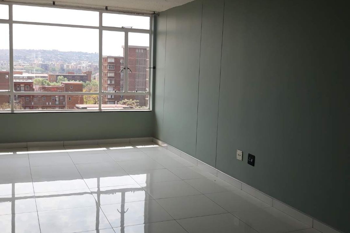 An empty living room featuring polished white floor tiles, a large window with city views, and a painted accent wall.