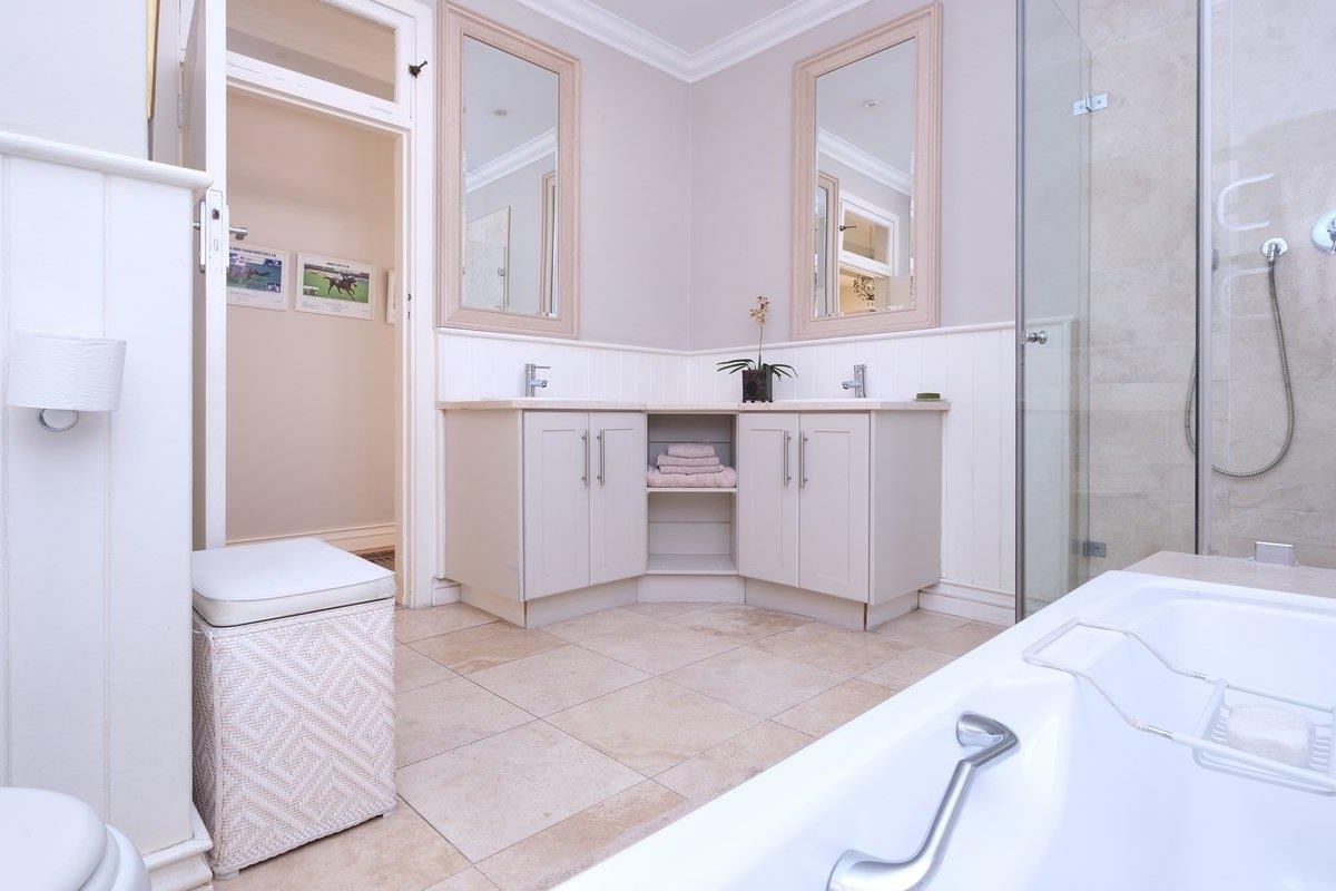 A well-maintained bathroom featuring a corner vanity with dual mirrors, a separate glass-enclosed shower, and a bathtub with tiled flooring.