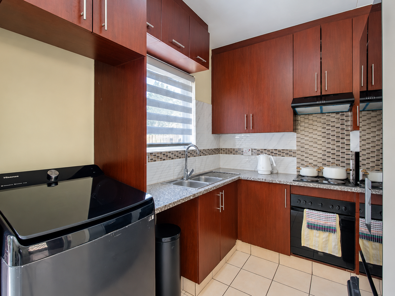A compact, functional kitchen featuring dark wood cabinetry, granite-look countertops, a mosaic tile backsplash, and integrated cooking appliances.