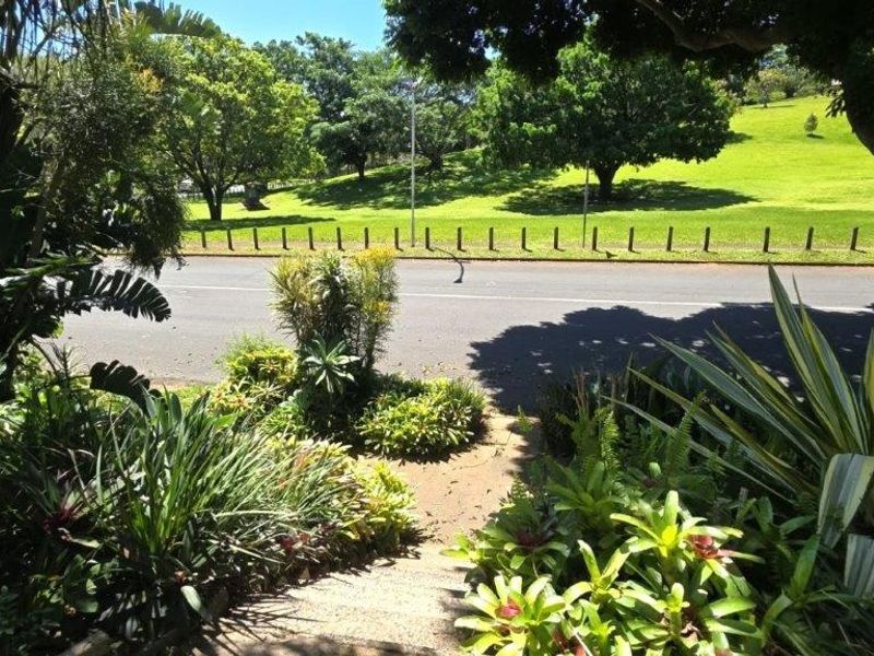 A view from the property looking out over a landscaped garden towards a quiet street and green parkland area.