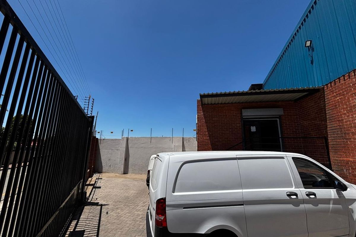 Exterior view of the property side yard featuring paved driveway, perimeter wall with electric fencing, and industrial-style brick building facade.