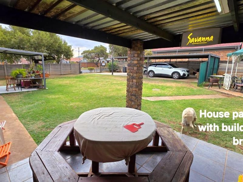 Covered patio area featuring tiled flooring, a brick support pillar, and a built-in braai, overlooking a spacious garden.