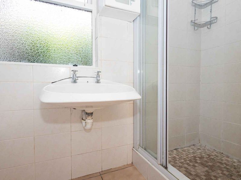 A functional bathroom featuring a wall-mounted basin, a tiled shower enclosure, and neutral wall tiling, ready for modernization.
