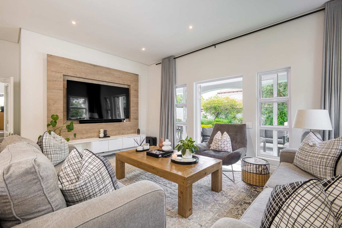 A bright and modern living room featuring a built-in wood-look media wall, recessed lighting, and large glass doors opening to a patio area.