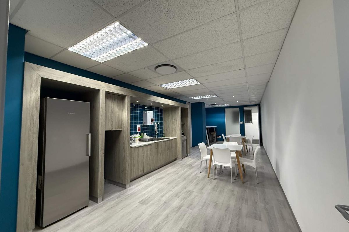 Modern office kitchenette featuring wood-grain cabinetry, tiled backsplash, stainless steel sink, and durable laminate flooring in a clean, professional workspace.