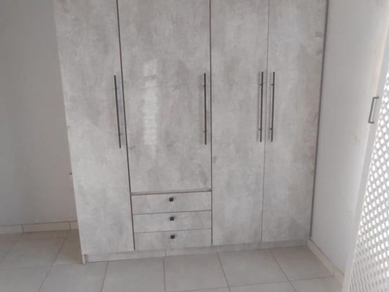 A bright bedroom featuring modern grey-toned built-in wardrobes and neutral tiled flooring throughout.