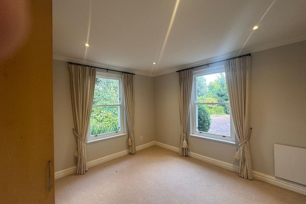 A bright and neutral bedroom featuring dual aspect sash windows, recessed downlighting, and wall-mounted heating, offering a clean and versatile living space.